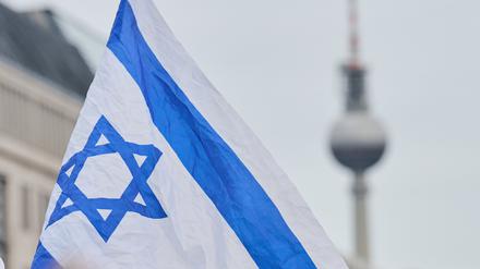 Eine Isreaflagge weht auf der Solidaritätskundgebung am Brandenburger Tor, während der Fernsehturm im Hintergrund zu sehen ist. 
