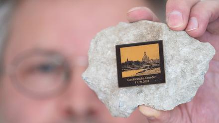Torsten Daae, Geschäftsführer im Dresdner Laden „Catapult“, hält einen Stein des abgerissenen Brückenteils der eingestürzten Carolabrücke mit einer Plakette in der Hand.