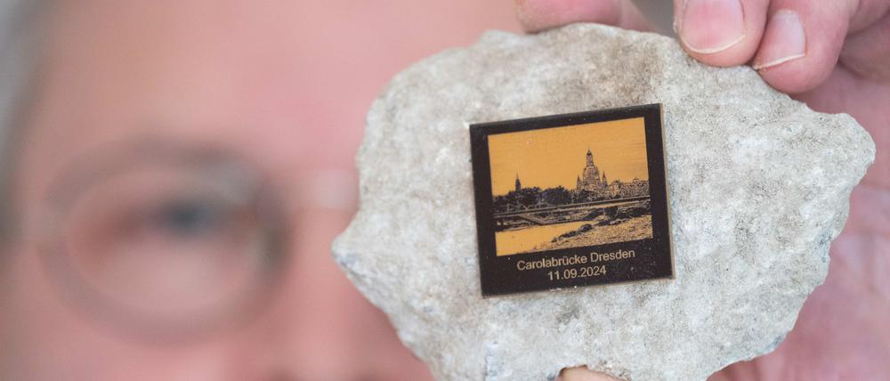 Torsten Daae, Geschäftsführer im Dresdner Laden „Catapult“, hält einen Stein des abgerissenen Brückenteils der eingestürzten Carolabrücke mit einer Plakette in der Hand.