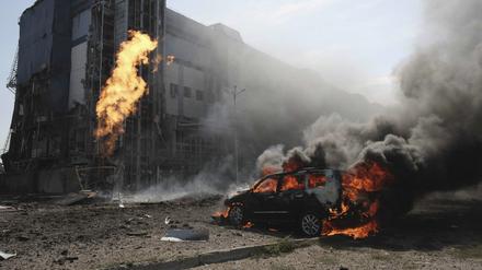 Nach zwei russischen Bombenanschlägen brennt ein Auto in Charkiw vor einem Geschäftszentrum, das durch die Angriffe beschädigt wurde. 