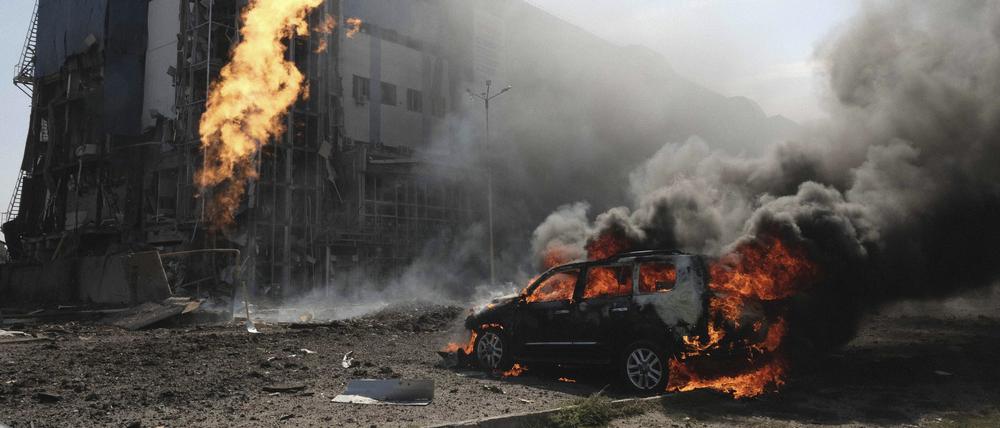 Nach zwei russischen Bombenanschlägen brennt ein Auto in Charkiw vor einem Geschäftszentrum, das durch die Angriffe beschädigt wurde. 
