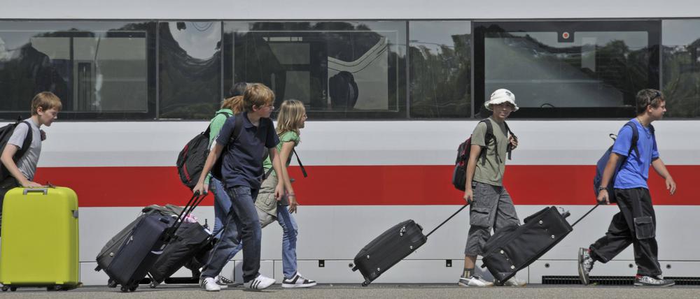 Reisende sind vor einem ICE-Zug in einem Bahnhof zu sehen.