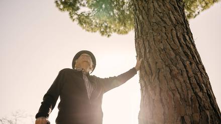 Ein alter Mann lehnt sich an einen Baum.