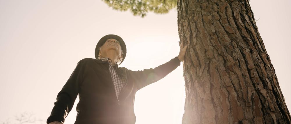 Ein alter Mann lehnt sich an einen Baum.
