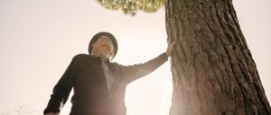 Ein alter Mann lehnt sich an einen Baum.