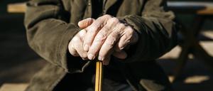  Die Hände des alten Mannes stützen sich auf seinen Gehstock.