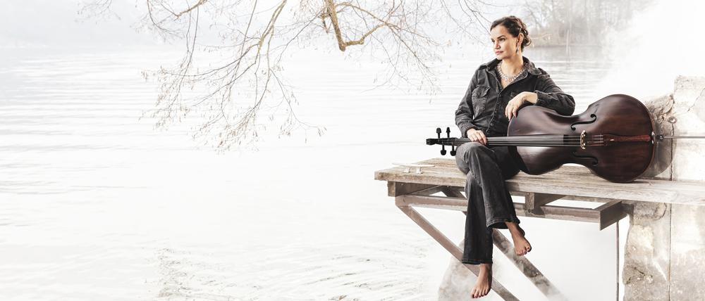 Die Cellistin Raphaela Gromes sitzt mit ihrem Instrument an einem See auf einem Steg.