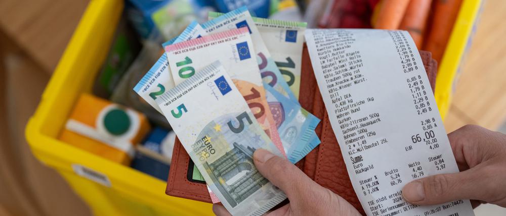 Eine Frau hält ein Portemonnaie mit Bargeld über einer Einkaufskiste mit Lebensmitteln. (Symbolfoto)