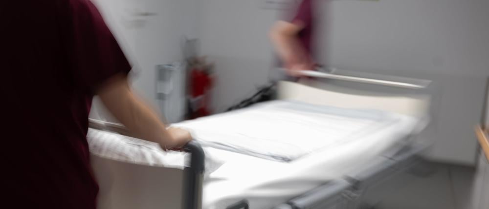 Eine Krankenpflegerin und ein Krankenpfleger schieben ein Krankenbett durch den Gang einer Station eines Krankenhauses.