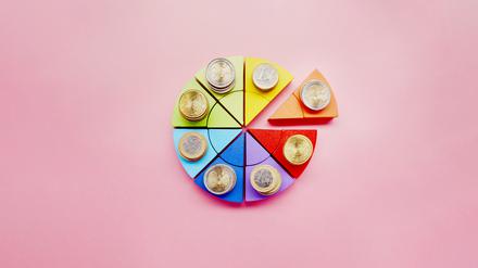 Kuchendiagramm aus bunten Bausteinen und Stapeln von Euro-Münzen auf rosa Hintergrund