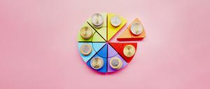 Kuchendiagramm aus bunten Bausteinen und Stapeln von Euro-Münzen auf rosa Hintergrund