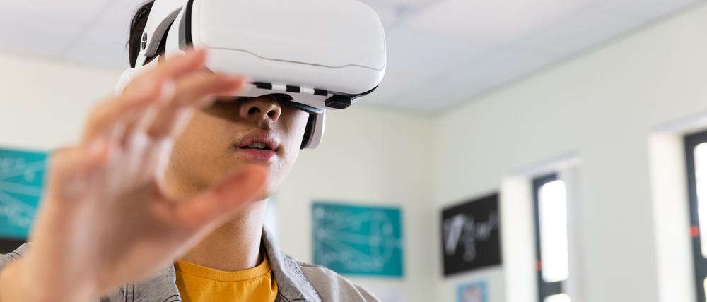Ein junger Mann trägt eine Virtual-Reality-Brille und streckt die Arme vor sich.