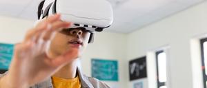 Ein junger Mann trägt eine Virtual-Reality-Brille  und streckt die Arme vor sich. 