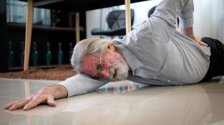 Ein älterer Herr liegt auf dem Boden und greift mit schmerzverzerrtem Gesicht an den unteren Rücken.