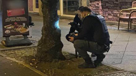 Zwei Polizisten begutachten eine Spur, die eine Kugel an einem Baum hinterlassen hat. Ein Mann war durch einen Schuss ins Bein verletzt worden. Am Abend sei er an einem Imbiss in Reinickendorf angeschossen worden, teilte ein Sprecher der Polizei mit. 