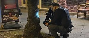 Zwei Polizisten begutachten eine Spur, die eine Kugel an einem Baum hinterlassen hat. Ein Mann war durch einen Schuss ins Bein verletzt worden. Am Abend sei er an einem Imbiss in Reinickendorf angeschossen worden, teilte ein Sprecher der Polizei mit. 