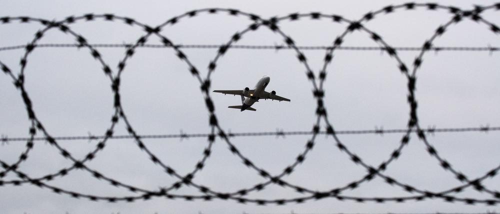 Ein Flugzeug startet am Flughafen Hannover – fotografiert durch Stacheldraht am Flughafenzaun.