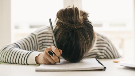 Woman writing on notepad resting her head on table