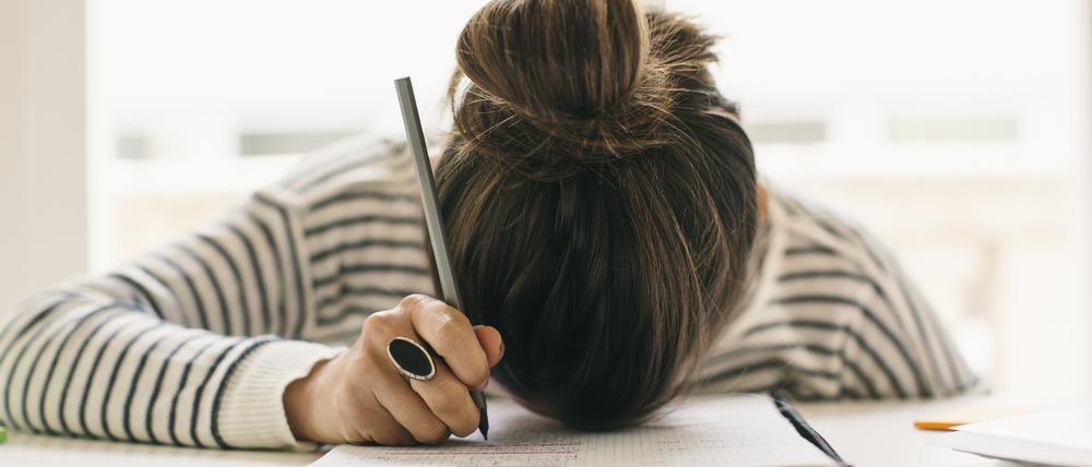 Woman writing on notepad resting her head on table