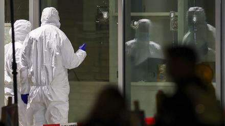 Polizeibeamte der Spurensicherung in weißen Schutzanzügen untersuchen Löcher in Glasscheiben des Kinos. 