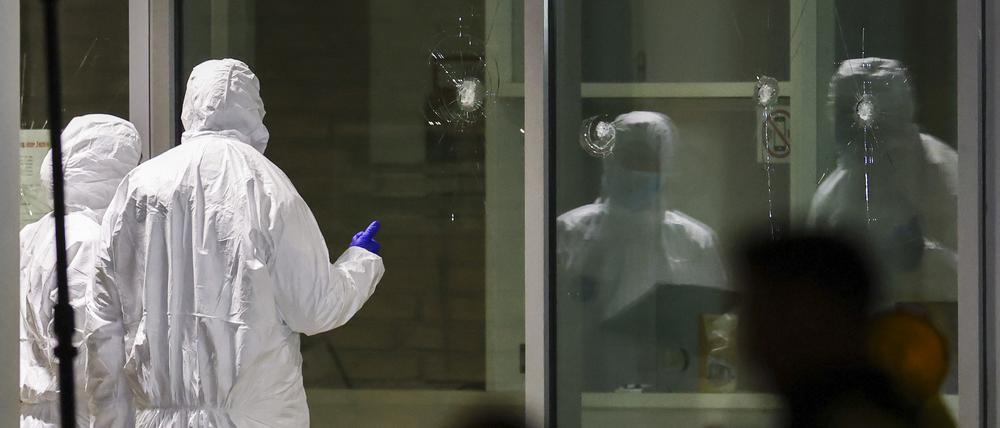 Polizeibeamte der Spurensicherung in weißen Schutzanzügen untersuchen Löcher in Glasscheiben des Kinos. 