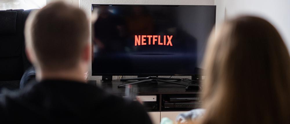 Ein Paar sitzt vor dem Fernseher, auf dem das Netflix-Logo zu sehen ist. 