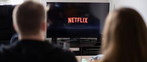 Ein Paar sitzt vor dem Fernseher, auf dem das Netflix-Logo zu sehen ist. 
