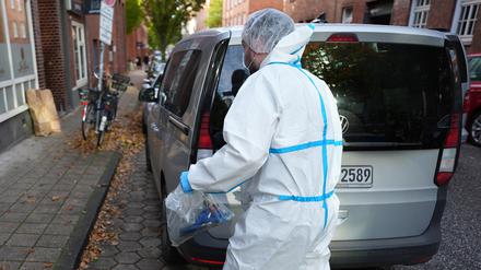 Ein Mitarbeiter der Kriminaltechnik steht an seinem Einsatzfahrzeug vor einem Mehrfamilienhaus in Hamburg.