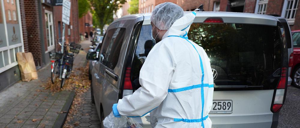 Ein Mitarbeiter der Kriminaltechnik steht an seinem Einsatzfahrzeug vor einem Mehrfamilienhaus in Hamburg.