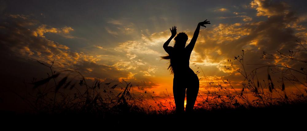 Eine Frau bewegt sich tänzerisch vor einem Sonnenuntergang.