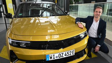 Florian Huettl, Geschäftsführer der Opel Automobile GmbH, hockt in der Unternehmenszentrale neben einem Opel Astra.