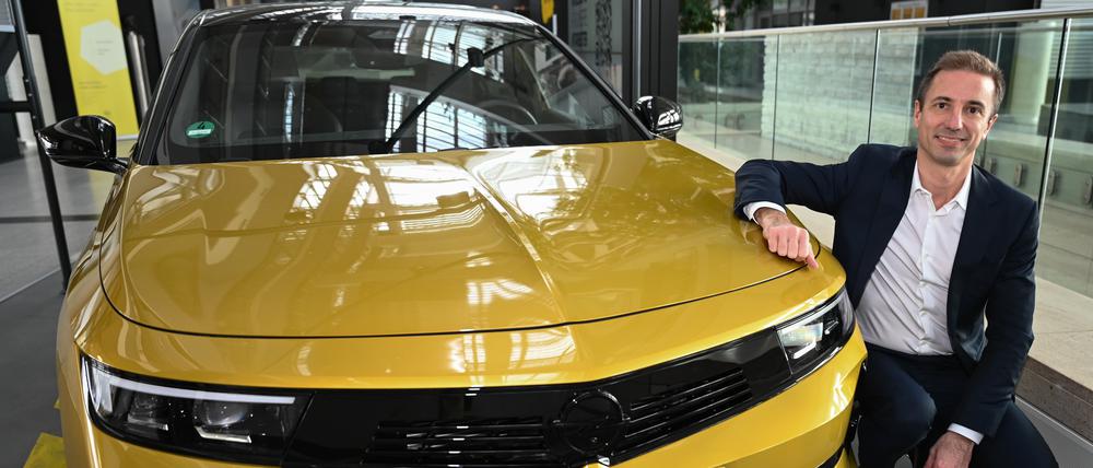 Florian Huettl, Geschäftsführer der Opel Automobile GmbH, hockt in der Unternehmenszentrale neben einem Opel Astra.