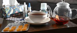 Medikamente und eine Kanne und Tasse Tee zur Bekämpfung einer Erkältung sind auf einem Nachttisch aufgestellt.