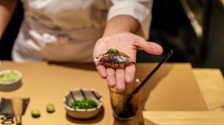 Symbolfoto: ein Mann hält ein Sushi in der flachen Hand. 