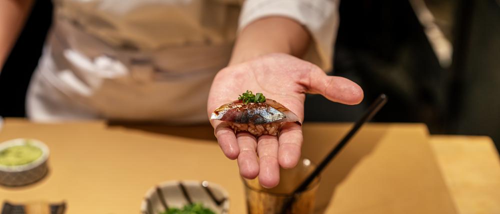 Symbolfoto: ein Mann hält ein Sushi in der flachen Hand.