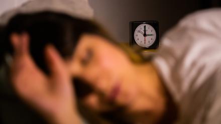 Eine Frau schläft neben einem Wecker, der auf drei Uhr zeigt (gestellte Szene). 