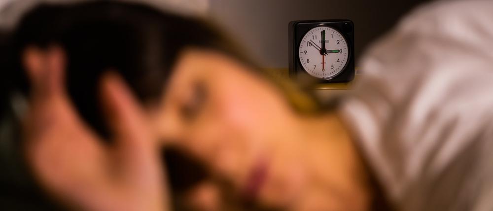 Eine Frau schläft neben einem Wecker, der auf drei Uhr zeigt (gestellte Szene).
