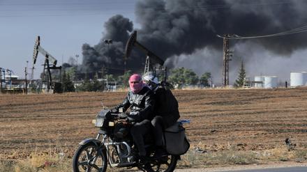 Menschen fahren auf einem Motorrad, während dichter Rauch aus einer Ölförderanlage aufsteigt, die am 25. Oktober 2024 nahe der nordöstlichen Grenze Syriens zur Türkei beschossen wurde (Archivbild).