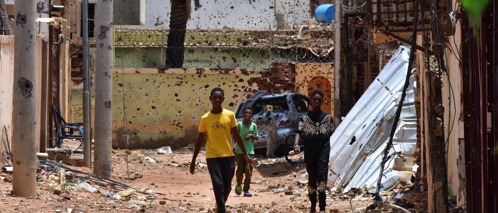 Jugendliche gehen auf einer von Zerstörungen gezeichneten Straße im Sudan.