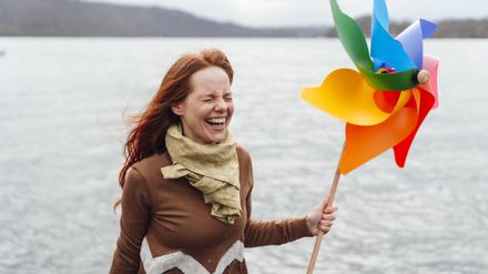 Woman holding pinwheel toy and laughing by lake.
