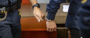 Ein Angeklagter wird von einem Polizisten mit einer Handschelle in den Verhandlungssaal geführt.