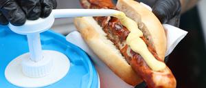 Senf wird auf eine Bratwurst im Brötchen gemacht.