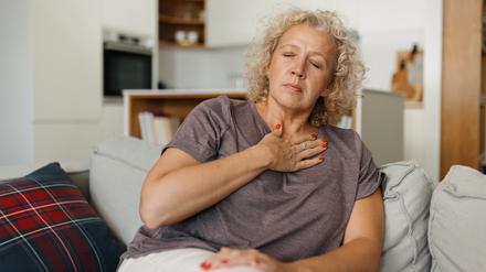 Eine Frau auf einem Sofa hält eine Hand vor die obere Brust (Symbolbild).