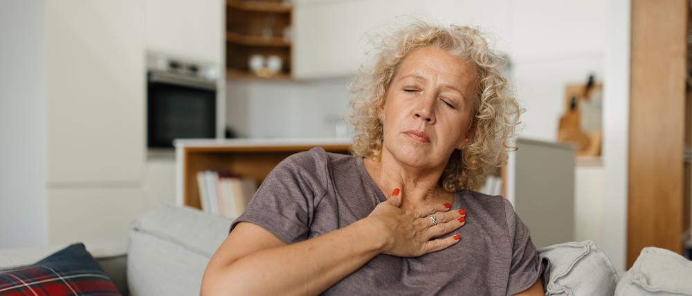 Eine Frau auf einem Sofa hält eine Hand vor die obere Brust (Symbolbild).