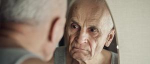 Ein alter Mann schaut grimmig blickend in den Spiegel.