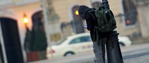 Ein Schulkind mit Schulrucksack steht angelehnt an einer Straßenlampe und ist mit einem elektronischen Spielgerät beschäftigt.