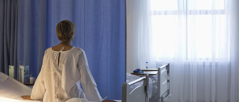 Eine Patientin sitzt auf einem Krankenhausbett und schaut aus dem Fenster.