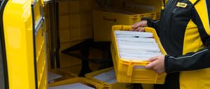 Eine Postzustellerin hält eine Kiste mit Briefen in der Hand.