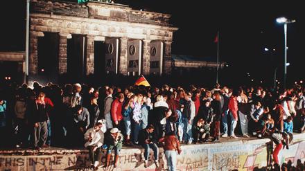 Jubelnde Menschen stehen am 09. November 1989 auf der Berliner Mauer vor dem Brandenburger Tor.