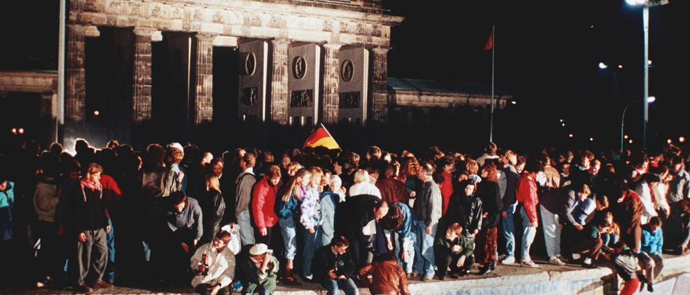 Jubelnde Menschen stehen am 09. November 1989 auf der Berliner Mauer vor dem Brandenburger Tor.